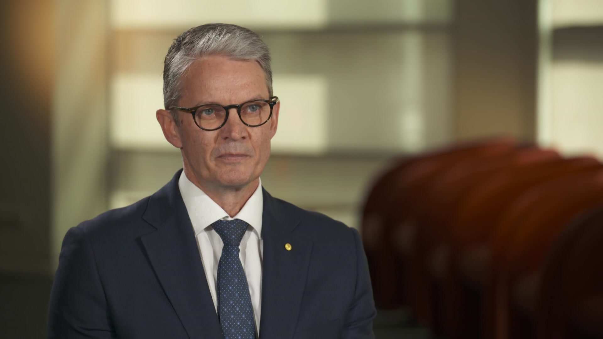 MCU of Prof. Brendan Crabb in a grey suit with white shirt and blue tie.